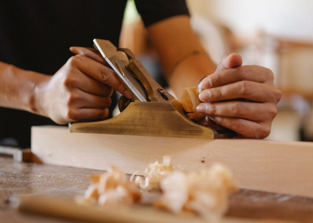 Close-up of hands using a wood smoothing plane on a wooden board.