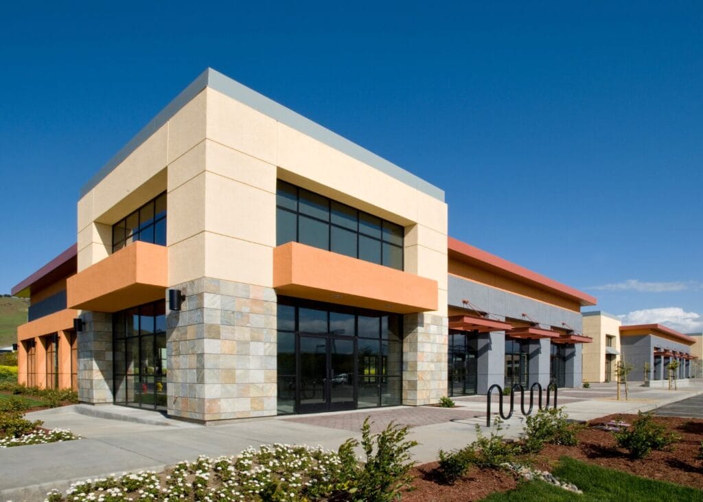 Modern commercial building with orange and gray facade, ample parking, and landscaping.